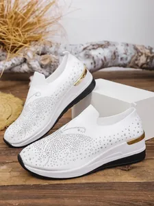 Detailed view of white fly-knit wedge sneakers with sparkling rhinestone accents.