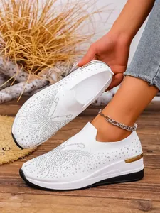 Detailed shot of white knit wedge sneakers decorated with sparkling rhinestone pattern