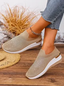 Close-up of beige flyknit wedge sneakers with rhinestone detailing and gold trim.
