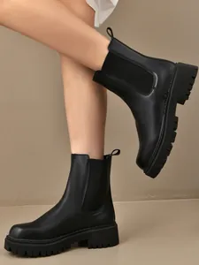Bottines Chelsea noires à semelles crantées portées par un mannequin avec style.