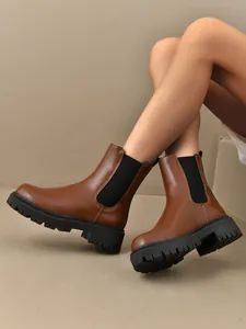 Gros plan de bottines Chelsea marron à plateforme et semelles épaisses sur jambes