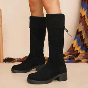 Close-up of stylish black suede knee-high boots with chunky heels and lace-up back detail