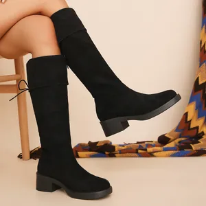 Side view of black suede knee-high stretch boots with chunky heels worn by model