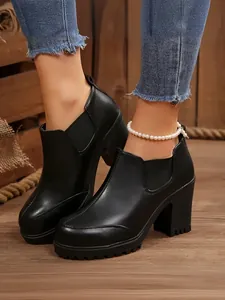 Close-up detail of women's black platform ankle boots with chunky heels and pearl anklet