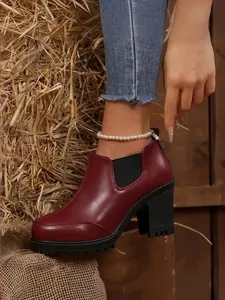 Close-up view of stylish burgundy chunky high heel platform boots worn in a rustic hay setting