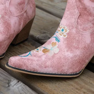 Detail view of pink distressed faux suede cowboy boots featuring floral embroidery