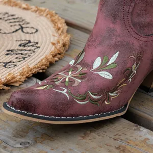 Close-up detail of floral embroidery on burgundy distressed leather western boot.