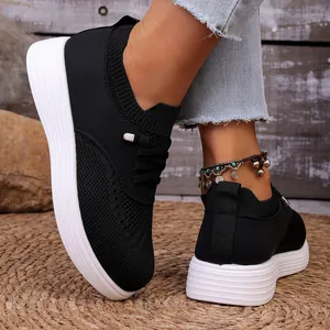 Vista laterale di sneaker nere in maglia con suola bianca spessa su un tappeto intrecciato