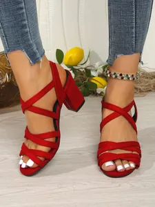 Vibrant red suede block heel sandals with elegant crisscross strap design on model.