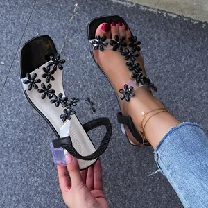 Close-up of transparent sandals featuring black flower ornaments and a clear block heel.