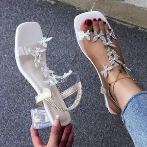Close-up of white block heel sandals with rhinestone butterfly straps and square toe.
