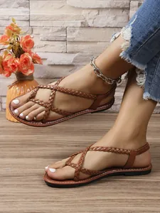 Vista lateral de sandalias planas trenzadas de color marrón para mujer en pies de modelo