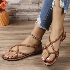 Primer plano de elegantes sandalias planas trenzadas de color marrón en los pies de mujer