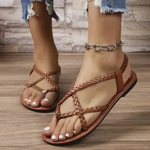 Primer plano de sandalias planas trenzadas de color marrón en los pies de una modelo.