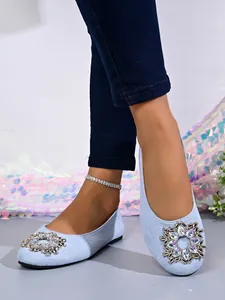 Detailaufnahme der hellblauen flachen Schuhe mit funkelnder Strassschnalle vorne.