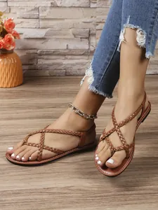 Primer plano de sandalias planas trenzadas marrones sobre un elegante suelo de madera