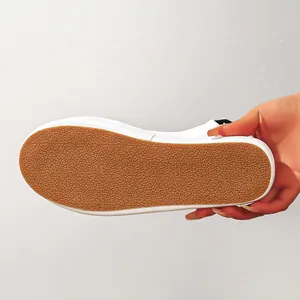 Close-up detail showing the anti-slip textured brown rubber sole of a white fashion sandal.