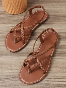 Detalle de sandalias de dedo trenzadas marrón con tira elástica sobre fondo de madera.