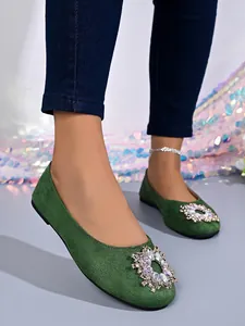 Detailansicht grüner flacher Schuhe mit glitzernder Strassschnalle und runder Kappe.
