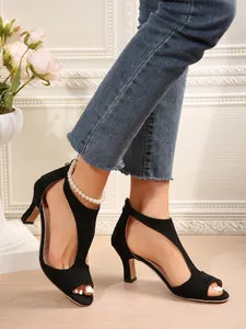 Detailed view of black suede peep-toe sandals with stiletto heels and pearl anklet