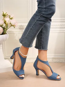 Close-up of denim blue peep-toe stiletto sandals featuring hollow-out sides and back zipper.