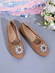 Detailansicht brauner flacher Schuhe mit funkelnden Kristallblumen-Schnallen und weicher Sohle.
