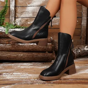Close-up side view of black leather Chelsea boots with chunky brown heel and zipper.