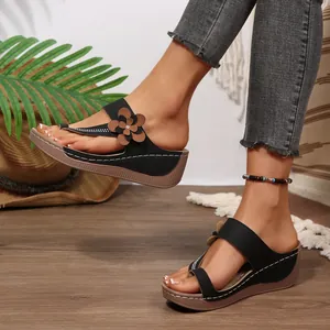 Detail view of stylish black wedge sandals featuring brown flower accent and thick sole.