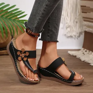 Stylish black wedge thong sandals with brown flower accent shown on feet outdoors.