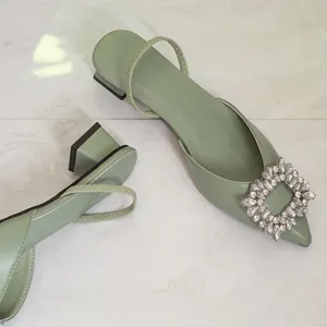 Close-up detail of elegant sage green pointed-toe slingback heels with square rhinestone buckle