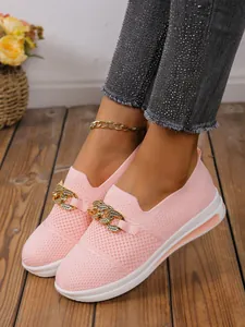 Detail van roze flyknit loafers met gouden ketting en strass-details op houten vloer.