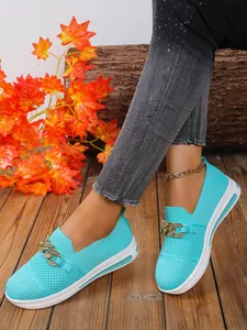 Close-up van cyaanblauwe flyknit loafers met goudkleurige ketting aan de voeten van het model