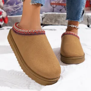 Close-up of tan platform snow boot slippers with embroidered trim on snow background.