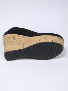 Detalle de zapato de cuña en ante negro con plataforma de corcho y suela ranurada.