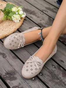 Detail view of beige hollow-out bow flats with floral laser-cut design on wooden deck