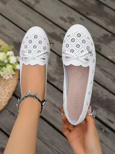 Detail view of white hollow-out flat shoes with bowknot and laser-cut floral pattern.