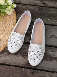 Detailed view of white hollow-out flats with decorative bow and rhinestone accents