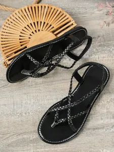 Gros plan de sandales plates tressées noires avec bride arrière élastique sur bois