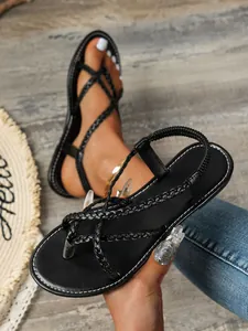 Détail de sandales plates noires à brides tressées avec bride arrière élastique.