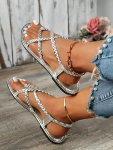 Gros plan sur des sandales plates tressées argentées pour femmes, style gladiateur.