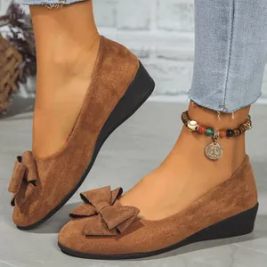 Detailed view of women's brown suede wedge shoes with a decorative bow on the toe