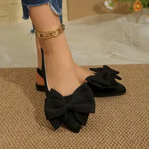 Detailed close-up of elegant black pointed-toe flat shoes with a large fabric bow