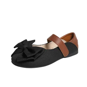 Detalle de bailarinas Mary Jane con lazo negro y correa de velcro en cuero marrón.