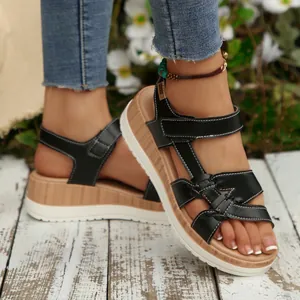 Close-up of black platform wedge sandals with velcro cross straps worn on a wood deck