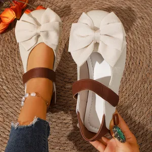 Detalle de bailarinas blanco roto con un lazo grande y una correa de velcro marrón.