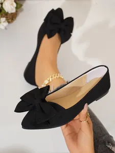 Elegant black pointed toe flats featuring a prominent decorative bow on the toe box.