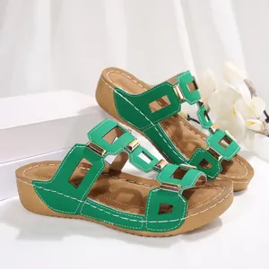 Detail van groene sleehak sandalen met gouden gespen en contrasterende stiksels.