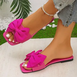 Close-up of vibrant fuschia flat sandals with a large textured fabric bow detail