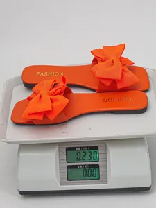 Vibrant orange flat bow sandals for women being weighed on a digital scale at 0.230kg
