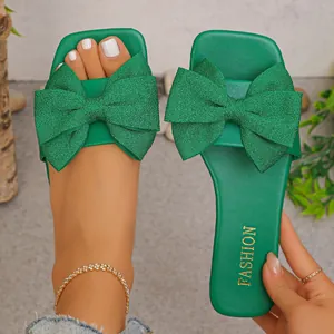 Detail of vibrant green flat sandals featuring a large glitter bow and square toe